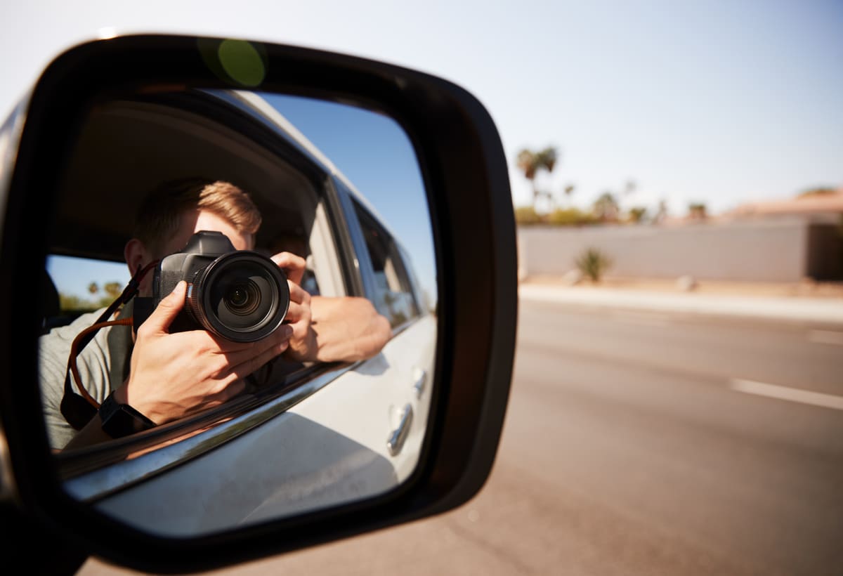 Investigator photographing activity from a vehicle mirror